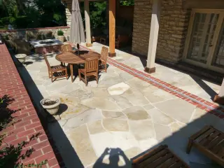 Flagstone patio with a red brick border beside a covered porch on a brick home